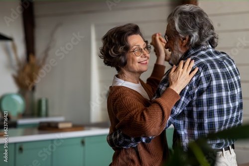 Happy elderly couple is laughing and dancing in the kitchen on their anniversary day. Old couple have emotional dance while listening good music