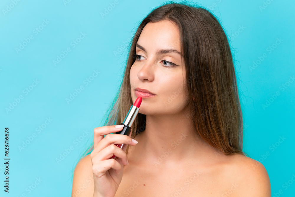 Young caucasian woman isolated on blue background holding red lipstick Young caucasian woman isolated on blue background holding red lipstick