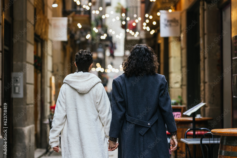 Obraz premium Couple of men walking away down an alley in the city holding hands.