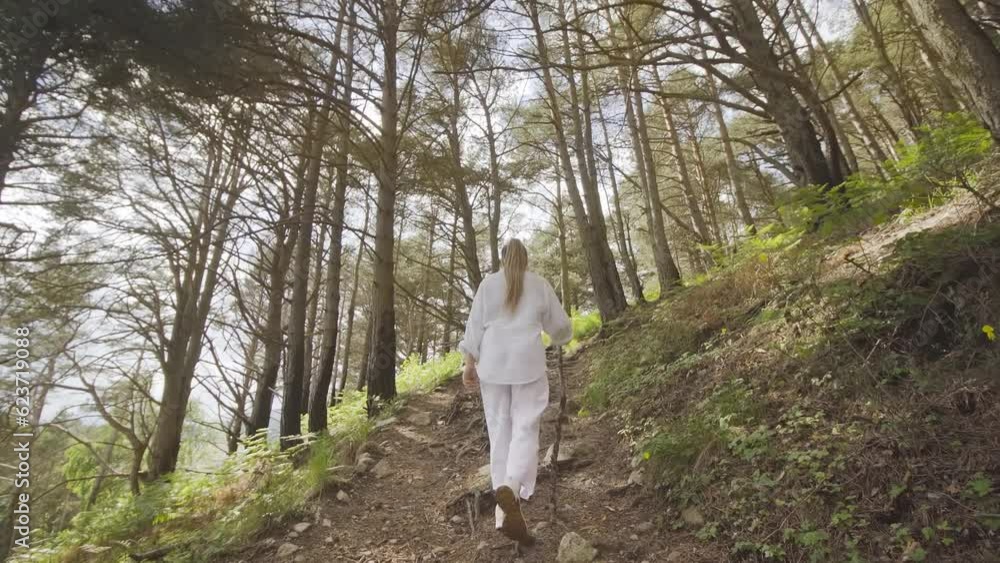 Woman in white walks in the woods with stick in hand Woman in white walks in the woods with stick in hand