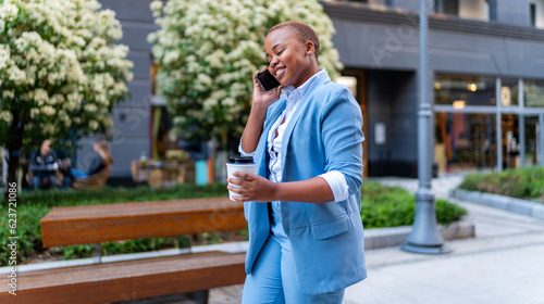 A young businesswoman walks to the office after a break with a coffee in her hand and talks on the phone