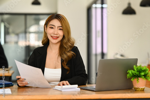 Portrait of asian woman investor using laptop and working on financial document in office