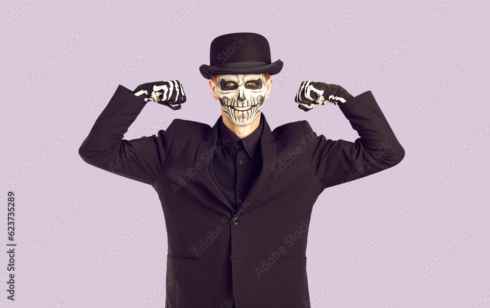 Zombie man with black and white face art shows muscles in studio. Isolated image on lilac background. Preparing for Halloween Party. Fashion model in day of dead costume. Zombie man with black and white face art shows muscles in studio. Isolated image on lilac background. Preparing for Halloween Party. Fashion model in day of dead costume.
