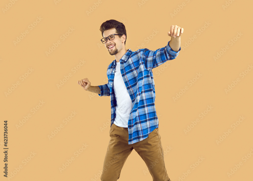 Portrait of happy excited young man dancing celebrating success. Attractive bearded optimistic man wearing glasses and blue plaid casual shirt having fun over isolated beige background Portrait of happy excited young man dancing celebrating success. Attractive bearded optimistic man wearing glasses and blue plaid casual shirt having fun over isolated beige background