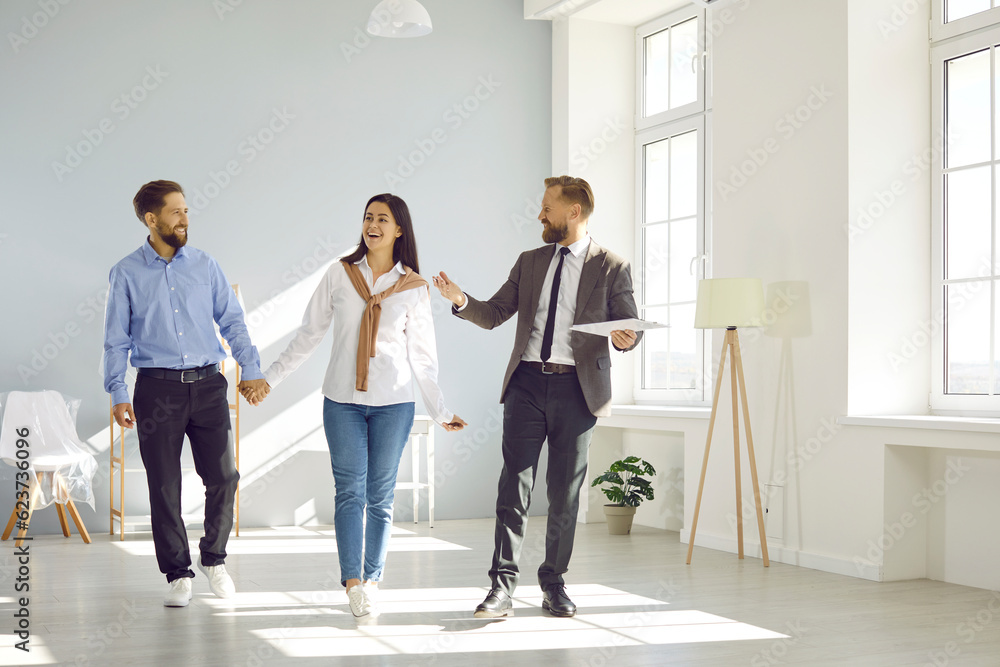 Fototapeta premium Real estate agent conducts tour for prospective tenants or potential home buyers. Happy man and woman are enthusiastically looking at house, holding hands and consulting with real estate expert.