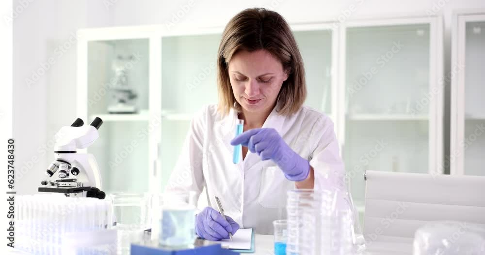 Scientist writes research report and test tube with blue liquid. Paperwork in the laboratory and chemical analysis of toxic liquids Scientist writes research report and test tube with blue liquid. Paperwork in the laboratory and chemical analysis of toxic liquids