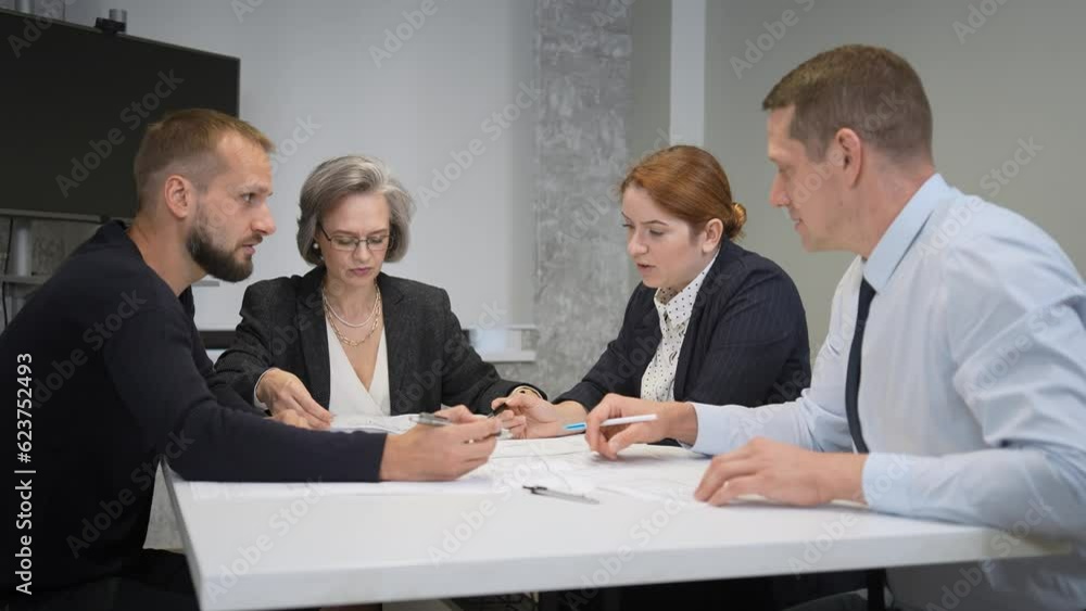 Four colleagues are discussing blueprints in a conference room in an office. Brainstorming of engineers and architects. Four colleagues are discussing blueprints in a conference room in an office. Brainstorming of engineers and architects.
