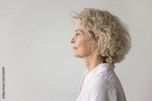 Obraz na plátně Thoughtful serious pretty blonde mature woman standing at white studio background, looking away in deep thoughts