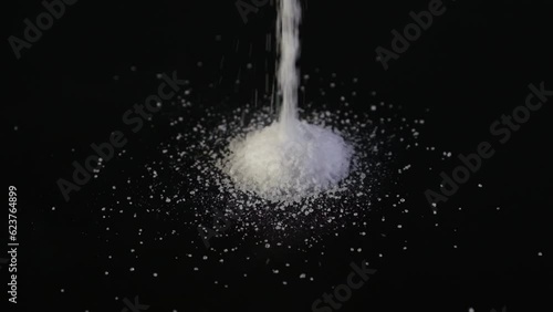 Aspartame powder falls on black surface. Food additive E951. Aspartame is an artificial non-saccharide sweetener 200 times sweeter than sucrose, used as sugar substitute in foods and beverages. photo