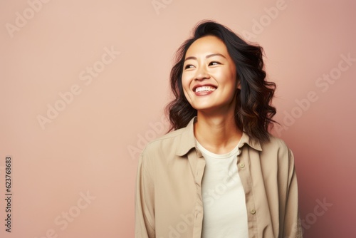 happy asian woman in beige jacket smiling at camera over pink background © Anne Schaum
