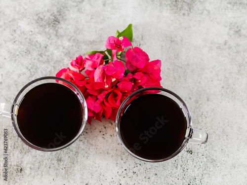 Top closeup shot of two black coffee cups with pink flowers over the wallpaper.