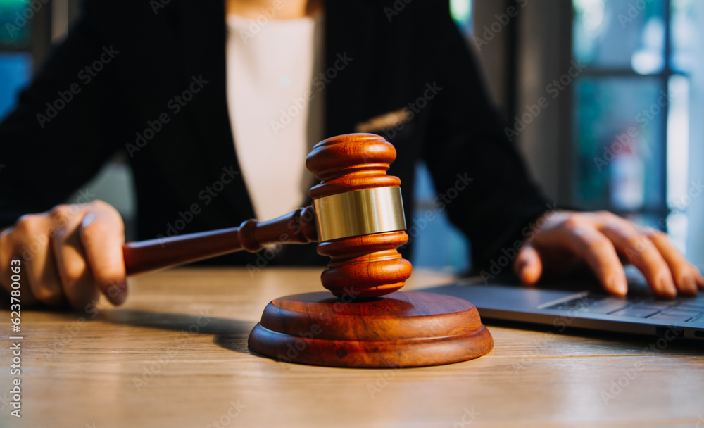 Justice and law concept.Male judge in a courtroom with the gavel, working with, computer and docking keyboard, eyeglasses, on table in morning light Justice and law concept.Male judge in a courtroom with the gavel, working with, computer and docking keyboard, eyeglasses, on table in morning light