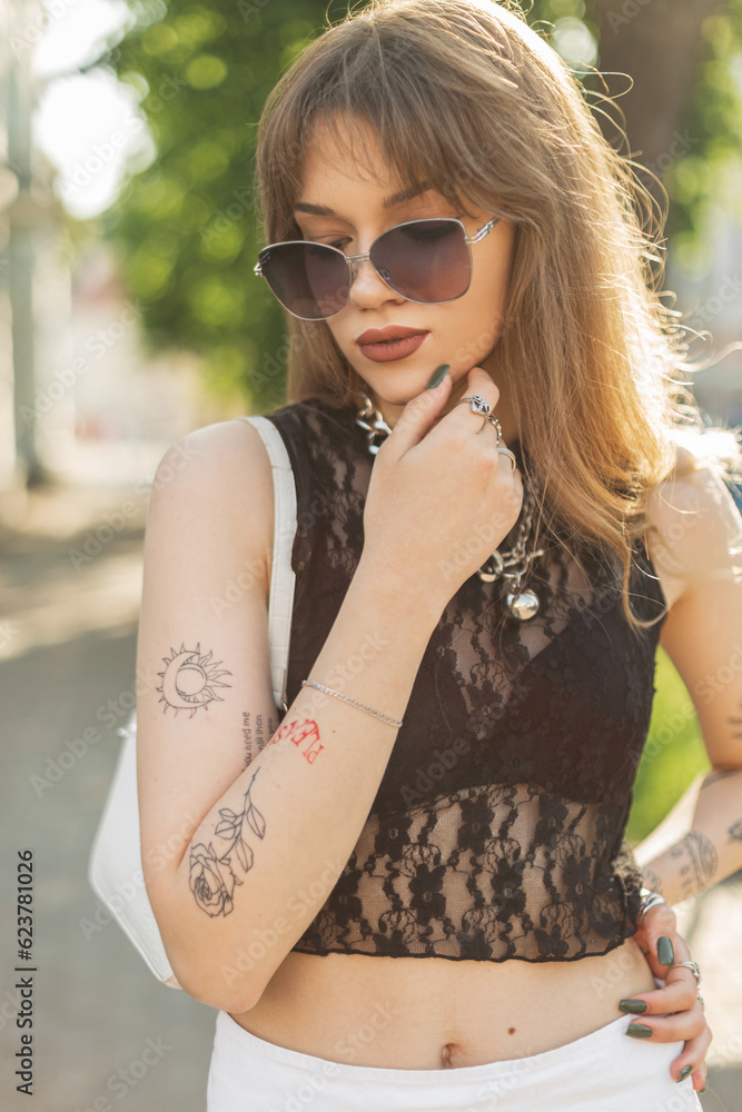 Beautiful trendy beauty hipster girl in fashion sexy outfit with sunglasses and a handbag walks in the city on a summer day Beautiful trendy beauty hipster girl in fashion sexy outfit with sunglasses and a handbag walks in the city on a summer day