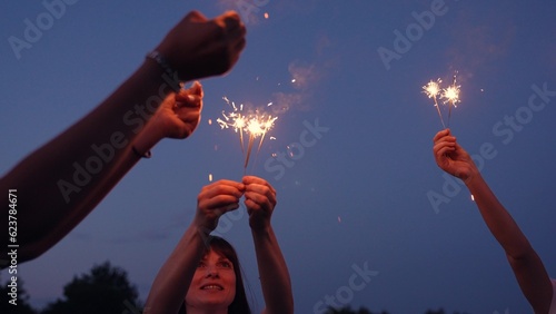 Fun party with bright sparklers, Glow Burn in your hands, bengal shimmer. Carefree girls students have fun outdoors against sky in evening. Holiday in nature at night, people have fun. Funky Celebrate