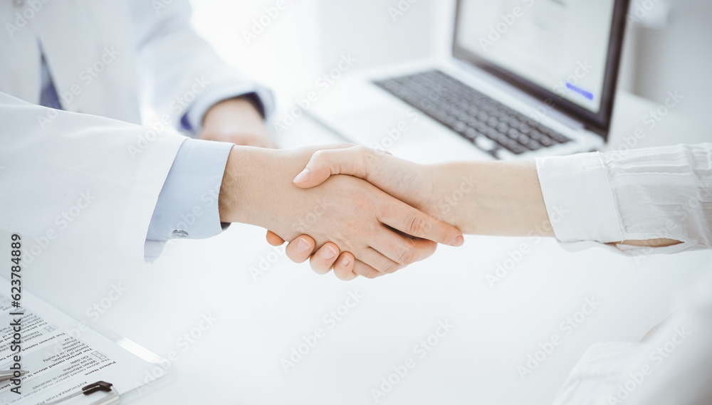 Doctor and patient shaking hands while sitting opposite of each other at the table in clinic, just hands close up. Medicine concept Doctor and patient shaking hands while sitting opposite of each other at the table in clinic, just hands close up. Medicine concept