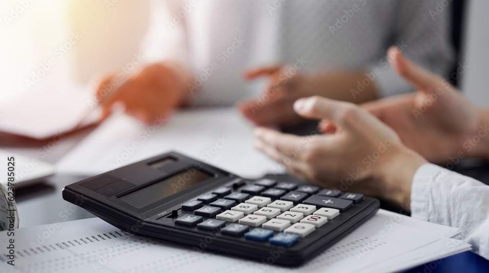 Woman accountant using a pen and laptop computer while counting and discussing taxes with a client, focus on the calculator. Business audit and finance concepts Woman accountant using a pen and laptop computer while counting and discussing taxes with a client, focus on the calculator. Business audit and finance concepts