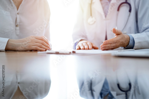 Doctor and patient discussing something while sitting near each other at the wooden desk in clinic. Medicine concept