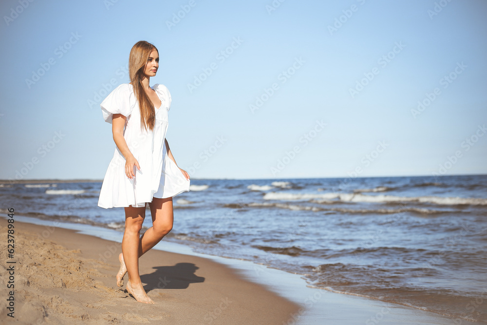 Happy smiling beautiful woman is walking on the ocean beach in a white summer dress Happy smiling beautiful woman is walking on the ocean beach in a white summer dress