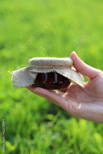 Hands holding a gars of jam near grass