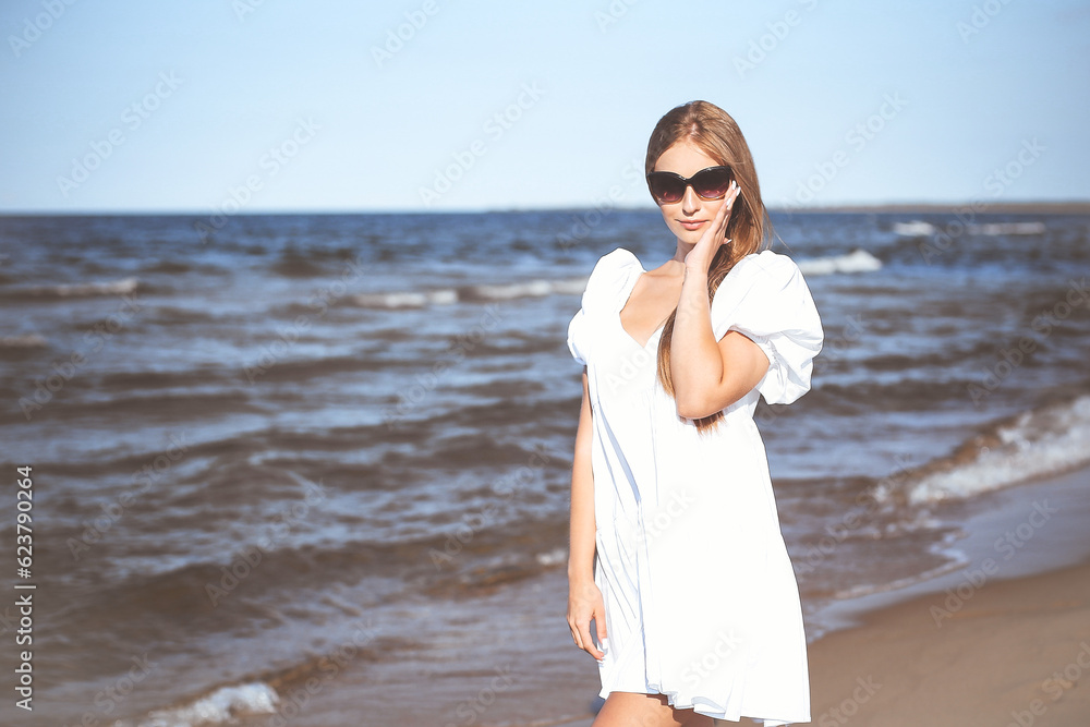 Happy smiling blonde woman is posing on the ocean beach with sunglasses Happy smiling blonde woman is posing on the ocean beach with sunglasses