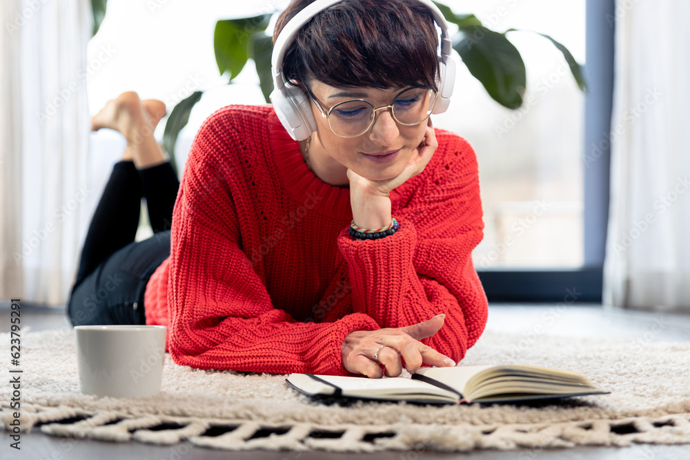 © leszekglasner - Listening music on headphones and reading a book on carpet at home floor