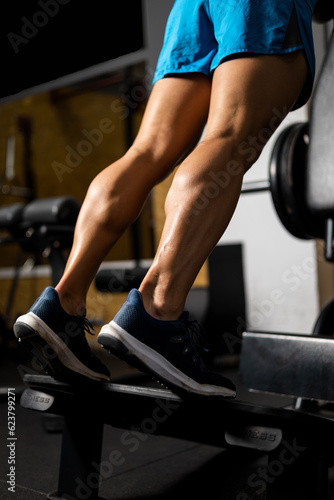 Vertical photo of an unrecognizable bodybuilder is working the twins or gastrocnemius on a machine inside a gym. Concept of working legs, strong calves, weight lifting with gastrocnemius.