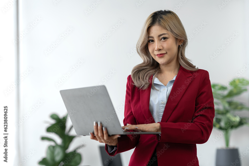 Portrait, Asian businesswoman or professional and confident female manager in standing suit holding a laptop computer to work, contact, search for business information online in the office Portrait, Asian businesswoman or professional and confident female manager in standing suit holding a laptop computer to work, contact, search for business information online in the office