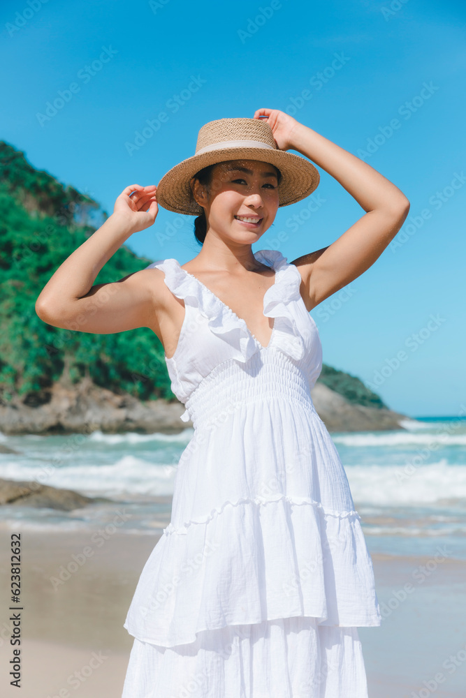 In perfect harmony with the sea, a woman in a white dress walks on the beach, experiencing the serenity and joy of the coastal surroundings.