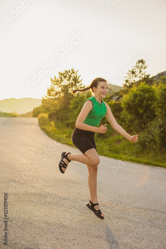 vertical portrait cute girl in tracksuit is engaged in sports activities on road surrounded by nature