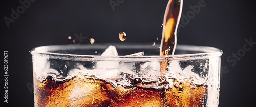Pouring of Cola and Ice. Cola soda and ice splashing fizzing or floating up to top of surface. Close up of ice in cola water. Texture of carbonate drink with bubbles in glass. Cold drink background photo