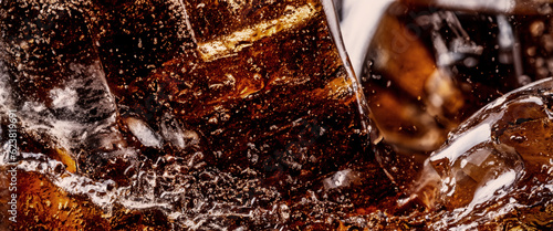 Pouring of Cola and Ice. Cola soda and ice splashing fizzing or floating up to top of surface. Close up of ice in cola water. Texture of carbonate drink with bubbles in glass. Cold drink background
