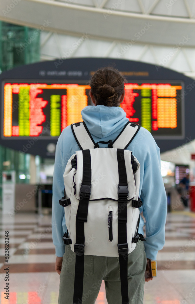 tourist with a backpack on the background of the board with a departure at the airport tourist with a backpack on the background of the board with a departure at the airport