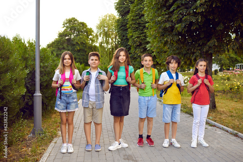 Back to school concept. Group of children with school bags. Outdoor portrait of several kids with backpacks. Six happy elementary students standing on a park path together