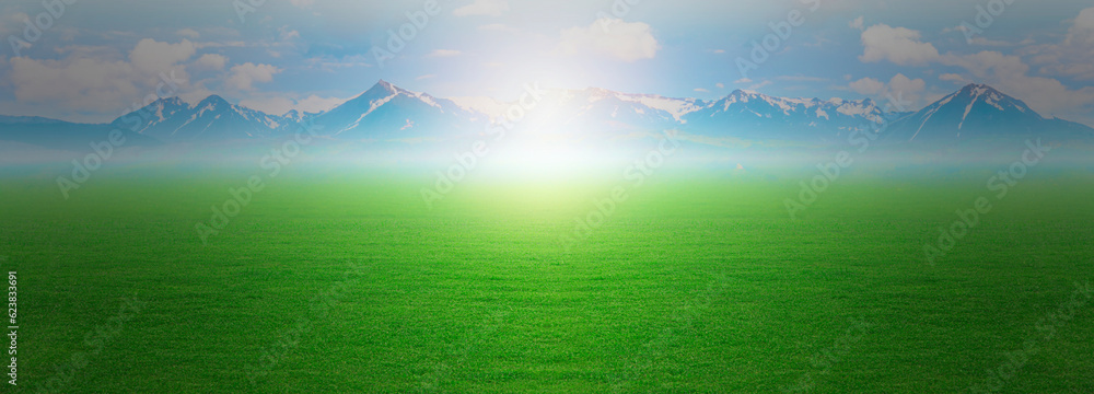 Landscape view of green grass and fog smoke with clouds and bright sun blue sky and mountain range in the background, summer spring meadow Landscape view of green grass and fog smoke with clouds and bright sun blue sky and mountain range in the background, summer spring meadow