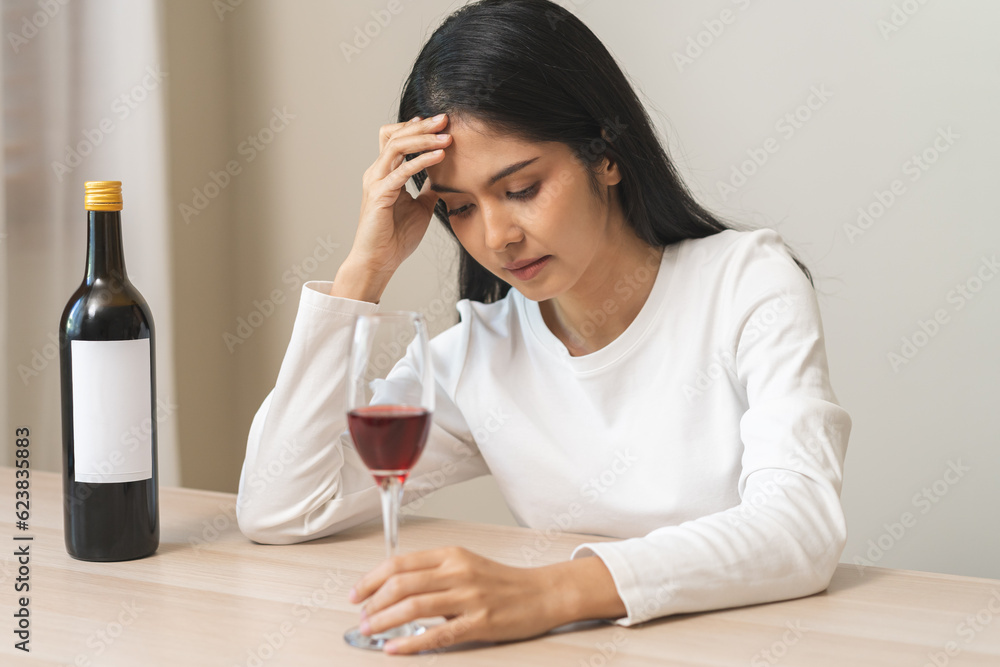 Alcoholism drunk asian young woman hand holding glass of red wine with whiskey bottle, female sitting alone, drinking on table at home. Treatment of alcohol addiction, suffer abuse problem alcoholism Alcoholism drunk asian young woman hand holding glass of red wine with whiskey bottle, female sitting alone, drinking on table at home. Treatment of alcohol addiction, suffer abuse problem alcoholism