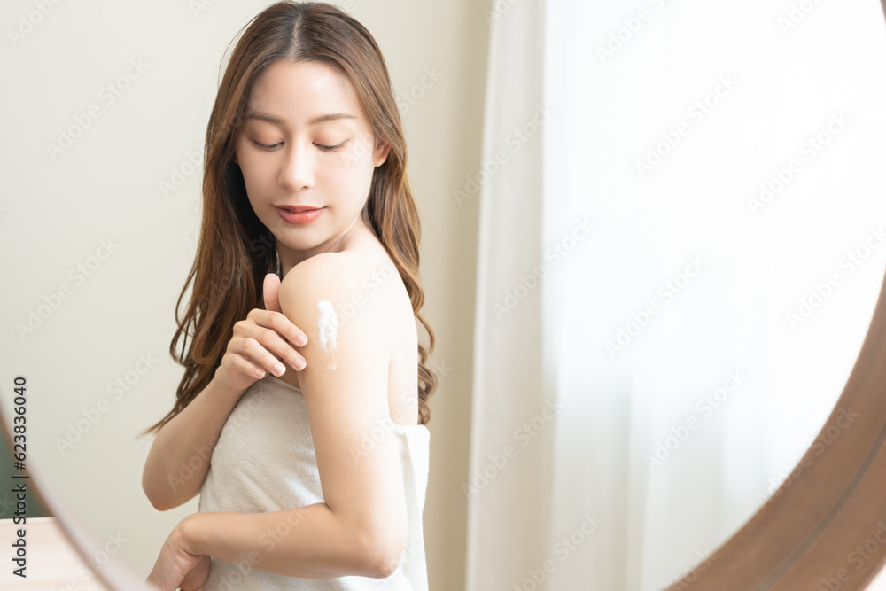 Health care, beauty smile asian young woman, girl wrapped in towel after shower bath looking in mirror at home, hand applying, putting moisturizing lotion on her shoulder. Skincare routine in morning. Health care, beauty smile asian young woman, girl wrapped in towel after shower bath looking in mirror at home, hand applying, putting moisturizing lotion on her shoulder. Skincare routine in morning.