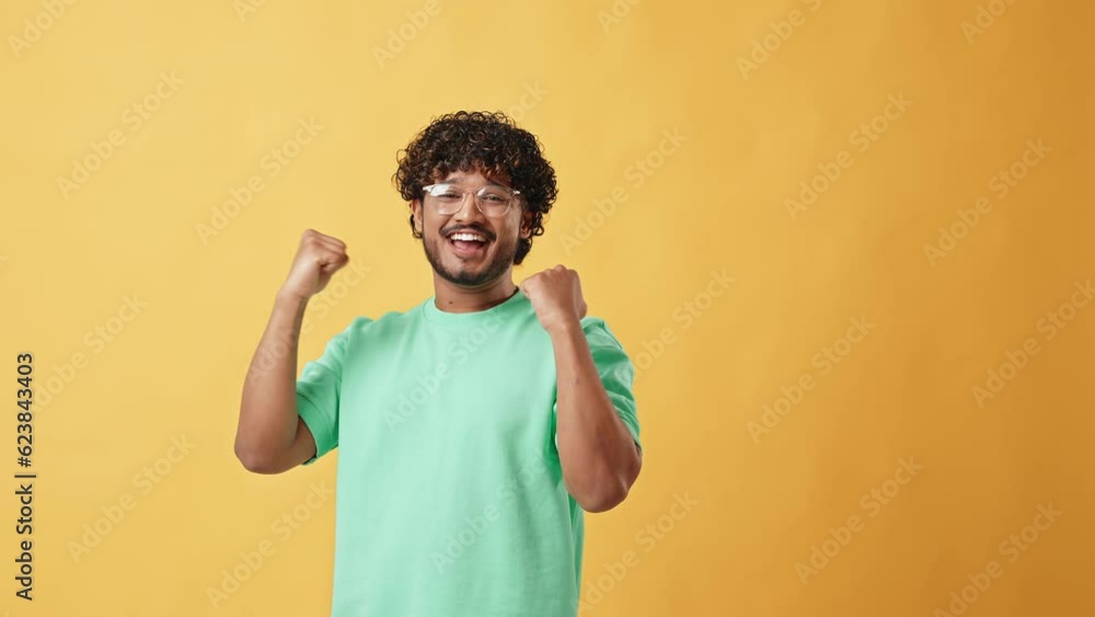 Happy, handsome, stylish young curly Indian man is sincerely happy and makes winning gesture while standing on yellow background. Enjoyment of victory, winning, luck. Happy, handsome, stylish young curly Indian man is sincerely happy and makes winning gesture while standing on yellow background. Enjoyment of victory, winning, luck.