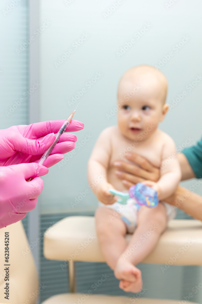 A doctor in blue gloves holds a syringe in an ampoule for vaccination against the background of a child, a baby, on a light background A doctor in blue gloves holds a syringe in an ampoule for vaccination against the background of a child, a baby, on a light background