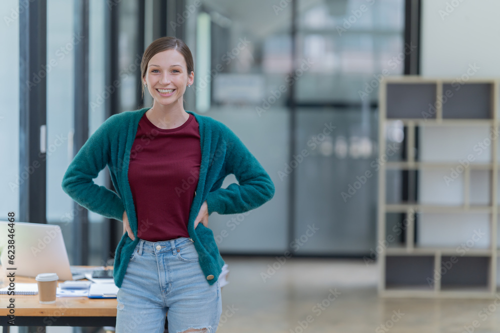 Obraz premium Sharing good business news. Attractive young businesswoman talking on the mobile phone and smiling while sitting at her working place in office and looking at laptop PC