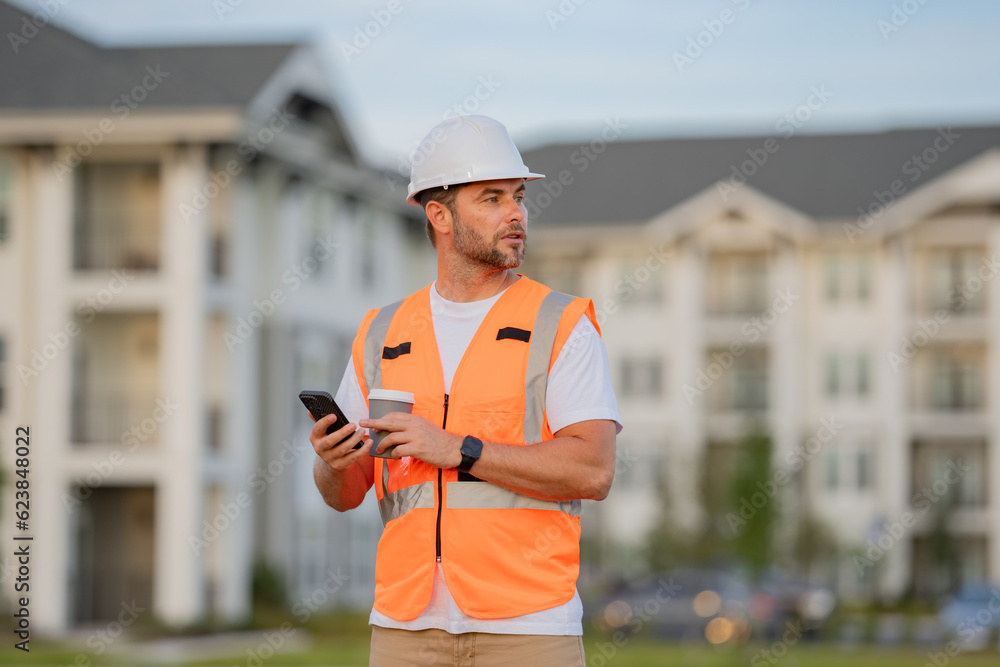 Engineer builder drinking take away coffee using phone on break. Builder on site construction. Man worker in hard hat. Construction worker in helmet at construction new home building. Engineer builder drinking take away coffee using phone on break. Builder on site construction. Man worker in hard hat. Construction worker in helmet at construction new home building.