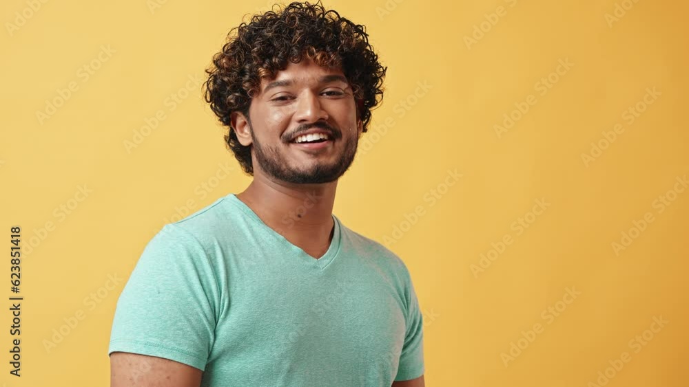 Advertising video portrait of a handsome curly-haired, adult, confident, modern Indian man standing on a yellow background, looking at the camera and smiling. Advertising video portrait of a handsome curly-haired, adult, confident, modern Indian man standing on a yellow background, looking at the camera and smiling.