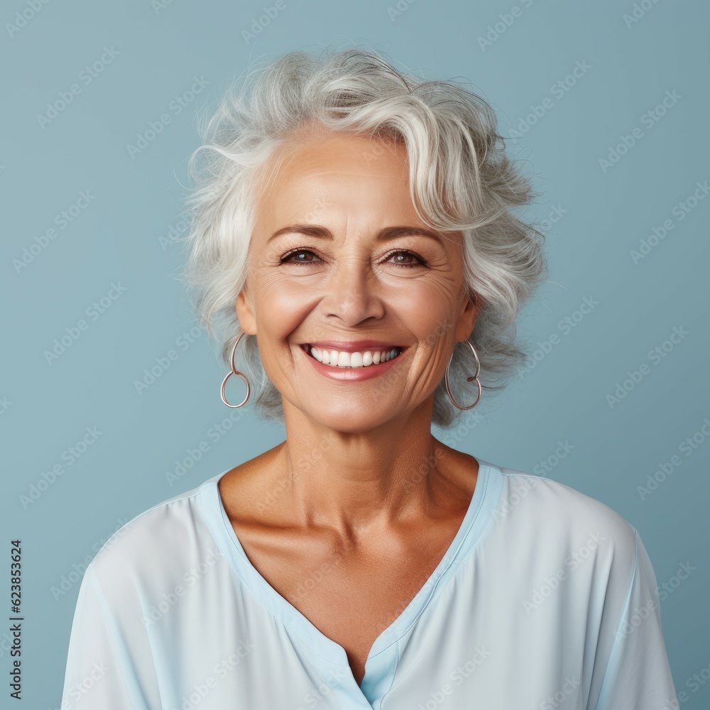 Portrait of a smiling senior woman with wavy gray hair on a blue background. Happy old Caucasian woman with a smile in a blue shirt looking at camera. Cheerful European woman with shiny white teeth. Portrait of a smiling senior woman with wavy gray hair on a blue background. Happy old Caucasian woman with a smile in a blue shirt looking at camera. Cheerful European woman with shiny white teeth.