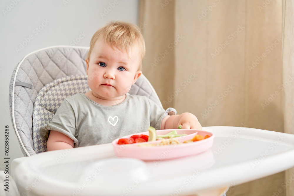 Cute child eats healthy food pasta and vegetables steamed,. Portraits of a cute 10 months old baby girl. The baby sitting in a special high chair for babies. Cute child eats healthy food pasta and vegetables steamed,. Portraits of a cute 10 months old baby girl. The baby sitting in a special high chair for babies.