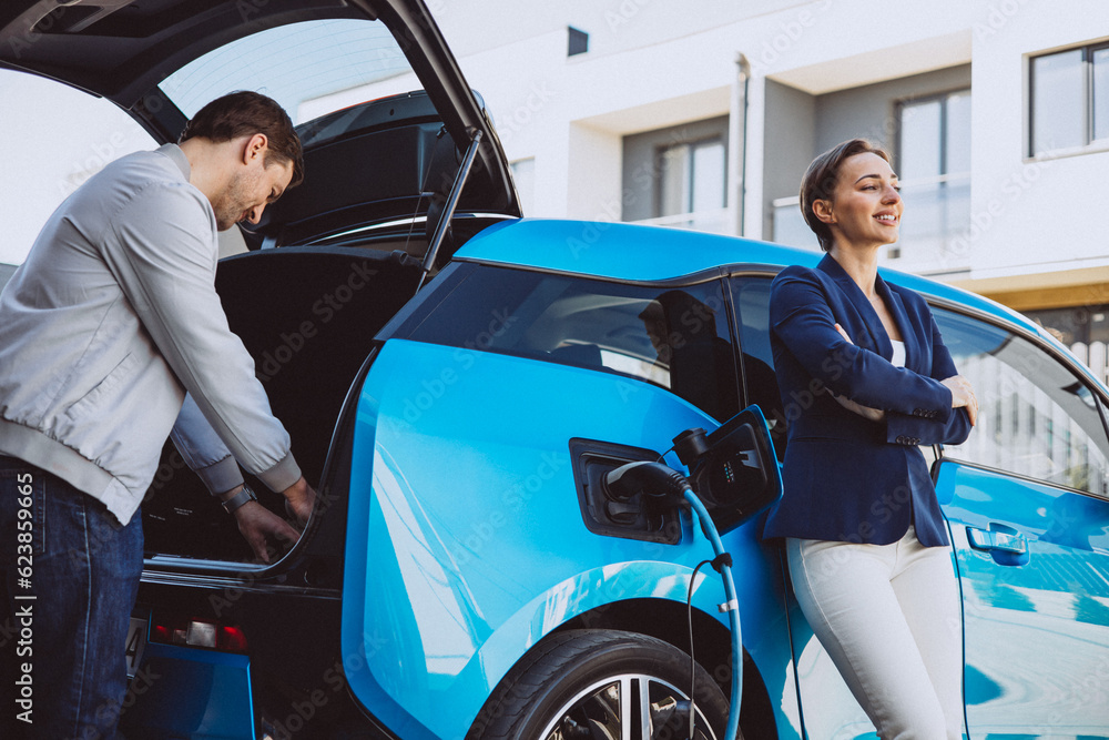 Couple talking by their electric car while its charging Couple talking by their electric car while its charging