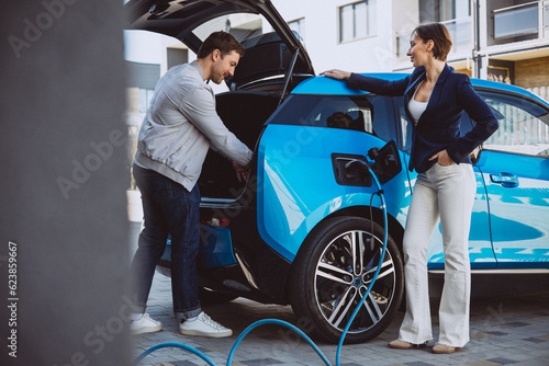 Couple talking by their electric car while its charging © Petro