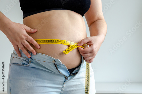 Overweighted woman measuring her belly with a measuring tape	
