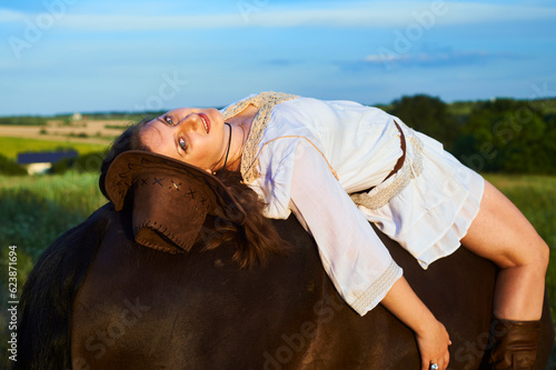 Beautiful girl laying on a horse on the sunset