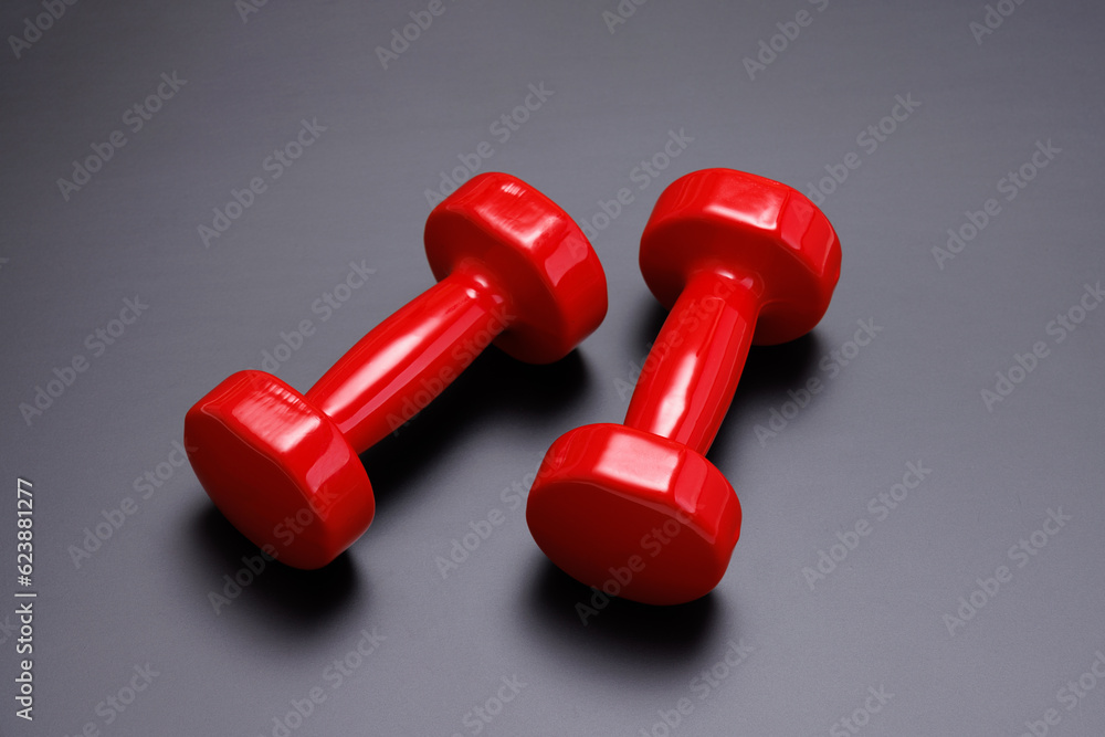 A pair of red dumbbells lies on a black matte surface. View from above. A pair of red dumbbells lies on a black matte surface. View from above.