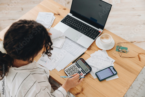 Photo Top view of a woman working at home in the kitchen with financial papers, counting on a calculator, paying bills, planning a budget to save some money