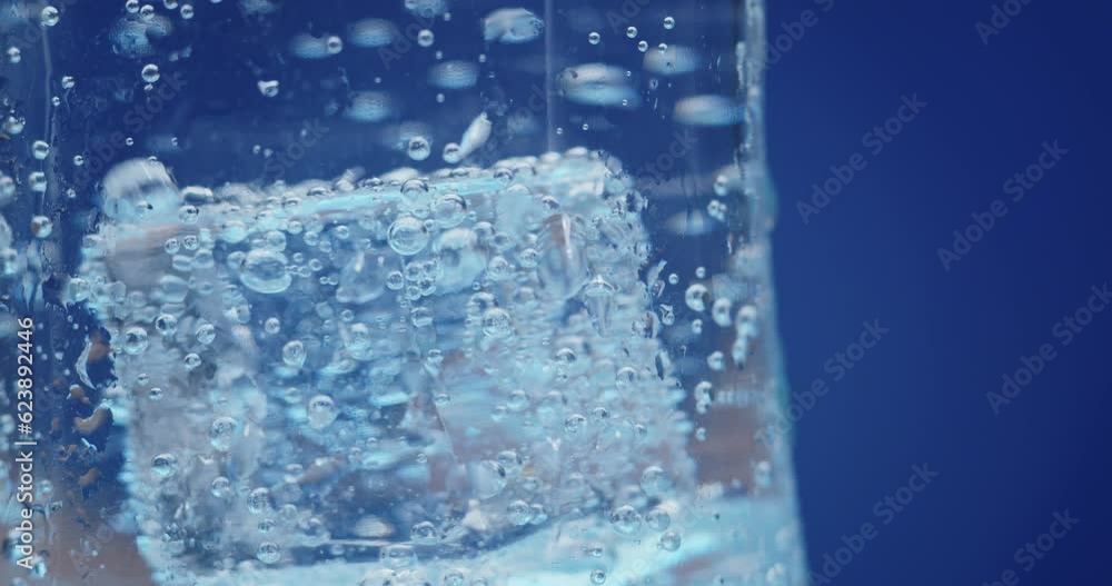 Ice cubes rotating in a glass with crystal clear water on a blue background. Refreshing and healthy water on hot days. Ice cubes rotating in a glass with crystal clear water on a blue background. Refreshing and healthy water on hot days.